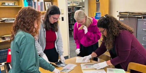 Three Franklin College students and Jessica Mahoney wear latex gloves and stand around a table working with documents and artifacts.