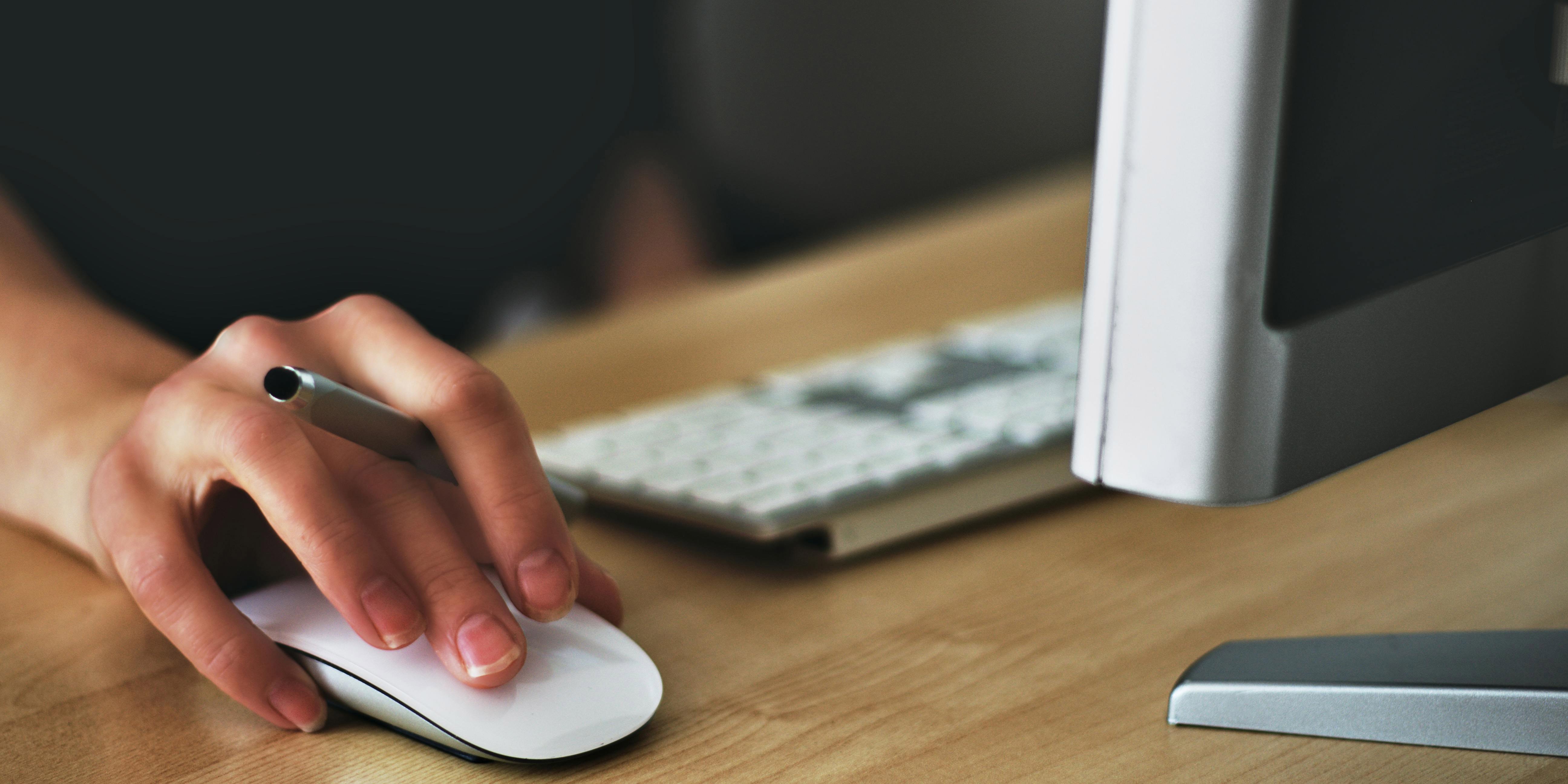 Close up of a hand on a computer mouse near a keyboard and screen